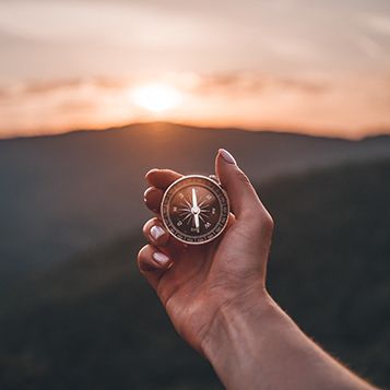 Woman hand with magnetic compass in summer mountains at sunrise,